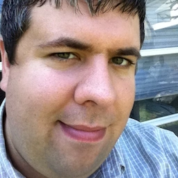 A headshot of Mike Zornek. Dark hair with grey speckles, green eyes and a cleanly shaven face.